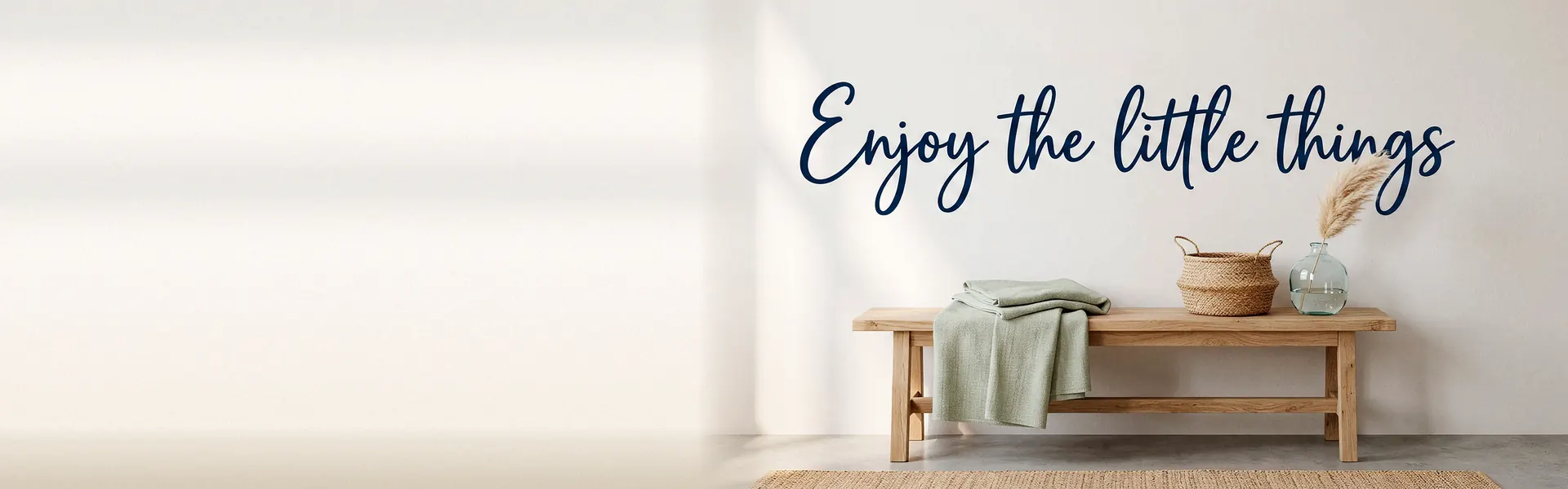 Frase «Enjoy the little things» en vinilo azul marino en la pared, encima de un banco de madera
